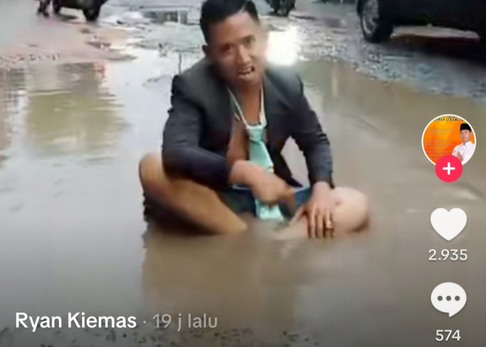 Sambil Duduk di Genangan Jalan Berlubang, Pemuda ini Kritik Jalan Rusak Bekas IPAL Palembang